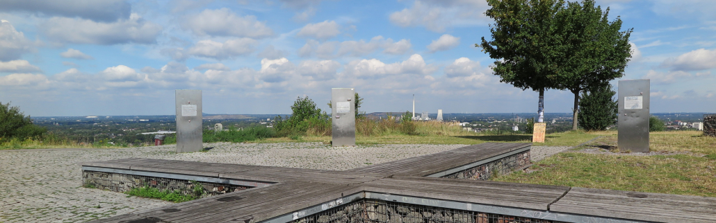 eine Kreuzförmige Holzbank auf der Spitze des Tippels Berges mit einer Aussicht über Bochum