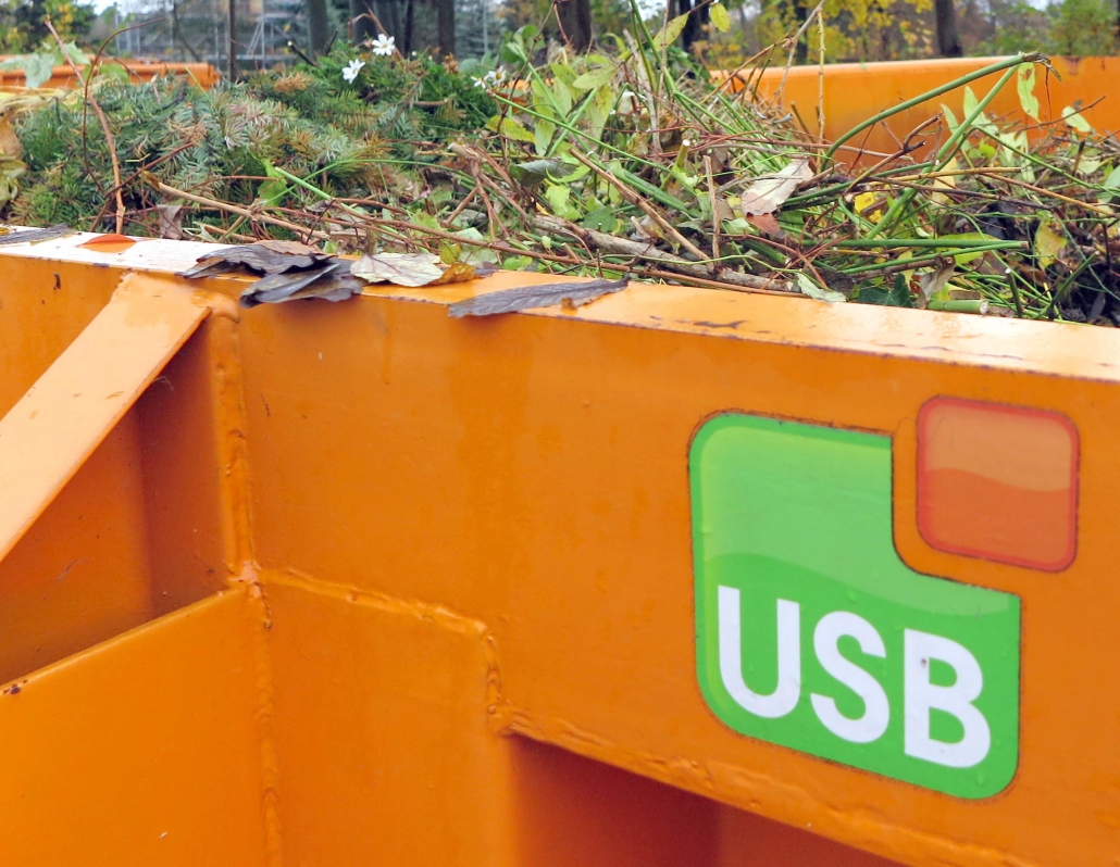 Ein orangener Container mit dem USB Logo, befüllt mit Grünschnitt