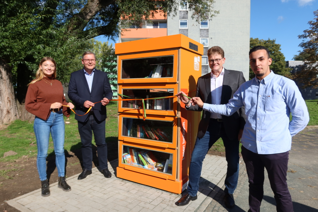 Buecherschrank Drei Männer und eine Frau eröffnen einen neuen Bücherschrank