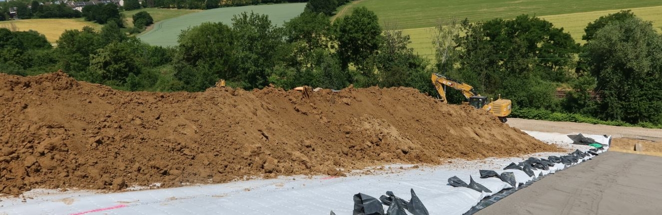 oberflaecehnabdichtung Erdhaufen liegen auf der Deponie. Im Hintergrund sieht man einen Bagger