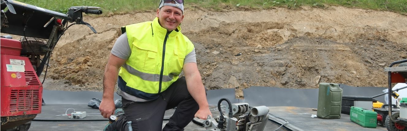 oberflaecehnabdichtung Arbeiter lächelt in Kamera und hält ein Baugerät in der Hand