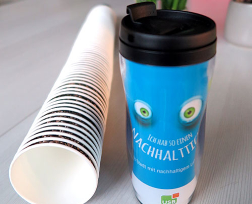 Becher Blauer Becher mit Augen steht neben liegenden Kaffeebecher