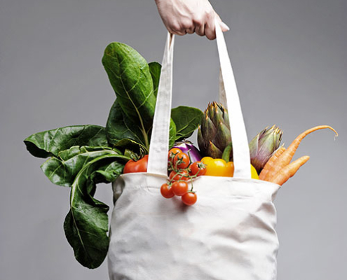 Cotton shopping bag overflowing with vegetables Eine Hand hält eine volle Einkaufstüte mit Gemüse