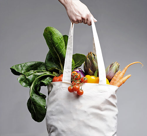 Cotton shopping bag overflowing with vegetables Eine Hand hält eine volle Einkaufstüte mit Gemüse