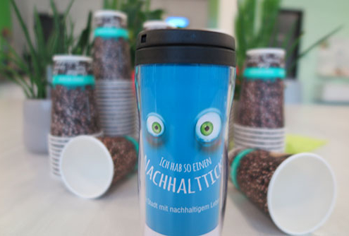 Becher Ein Blauer Becher mit Augen. Im Hintergrund sind Coffe-to-go-Becher