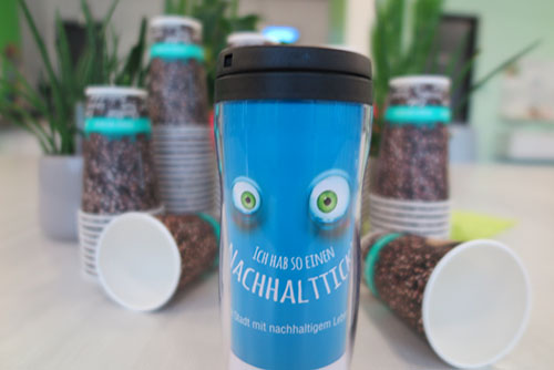 Becher Ein Blauer Becher mit Augen. Im Hintergrund sind Coffe-to-go-Becher