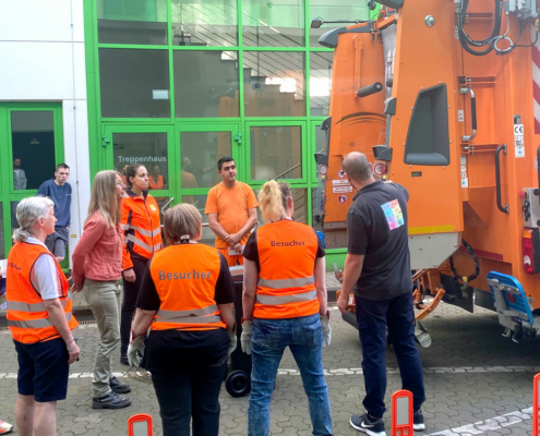 Matchday Orange gekleidete Personen stehen hinter einem Müllwagen und beobachten diesen