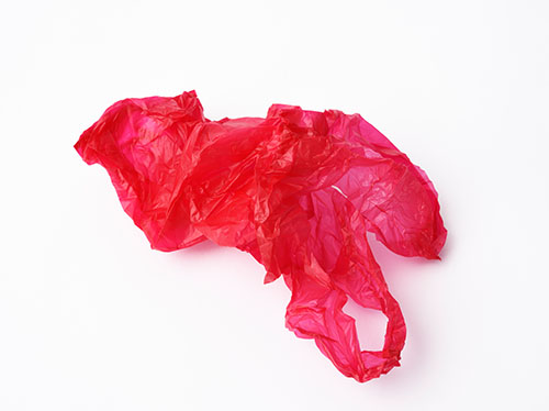 Crumpled red plastic shopping bag on white background Rote Plastiktüte liegt auf dem Boden