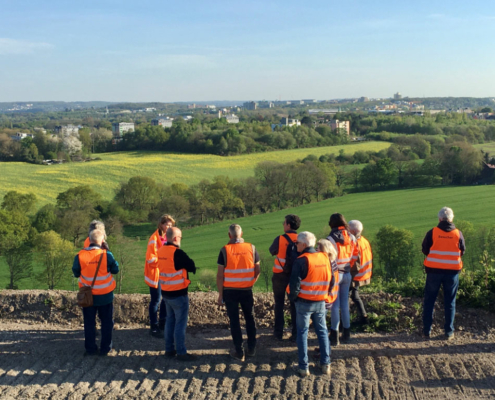 baustellenfuehrungen Orange gekleidete Menschen schauen auf eine Grünfläche