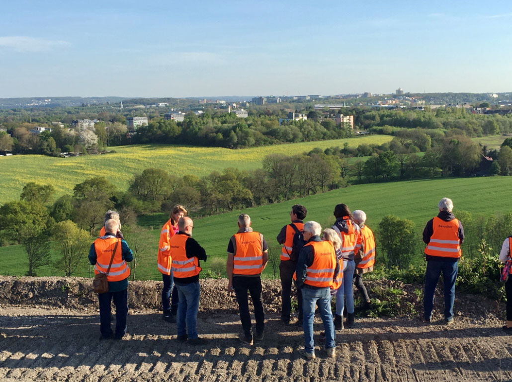 baustellenfuehrungen Orange gekleidete Menschen schauen auf eine Grünfläche